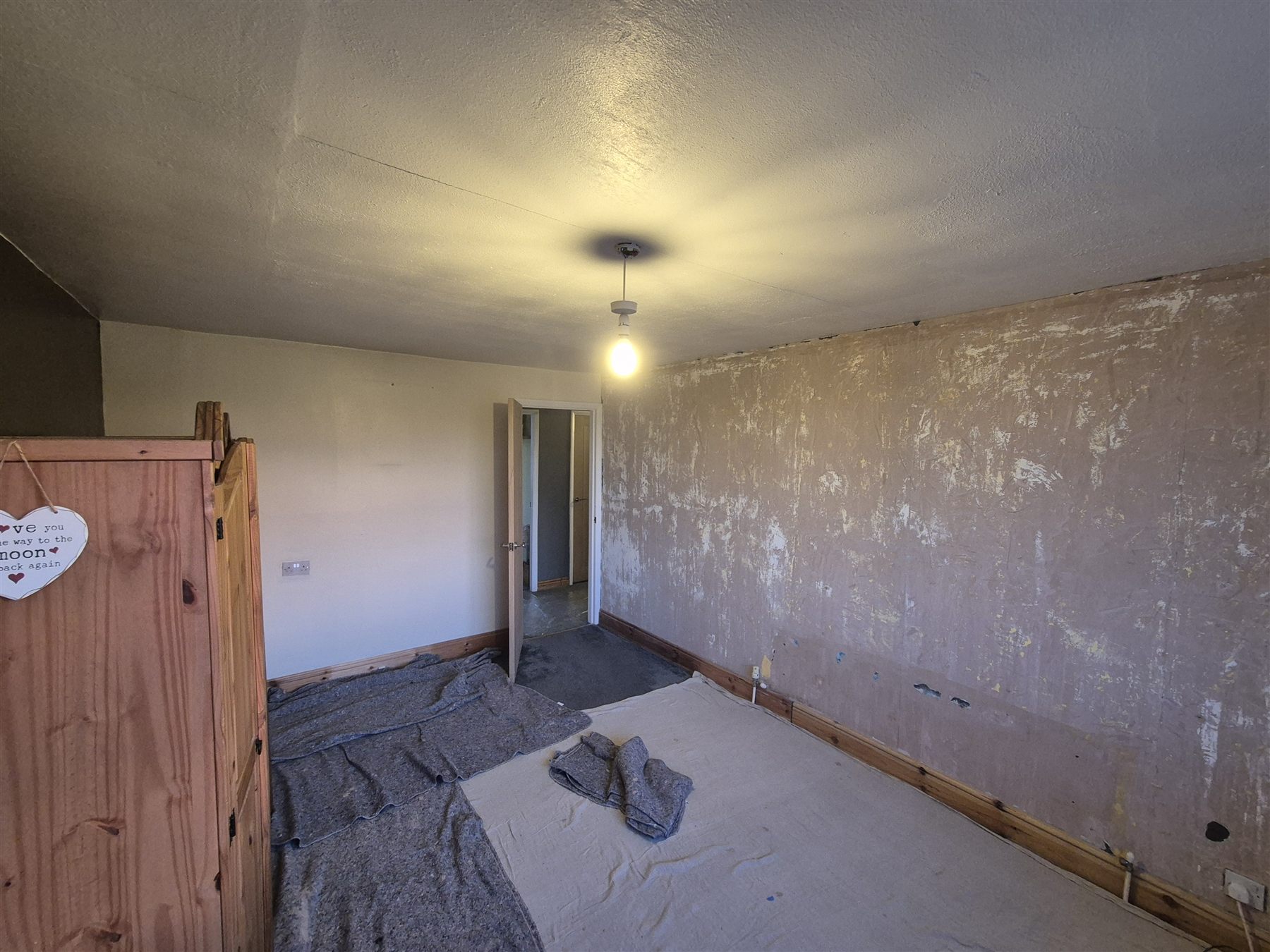 Bedroom with worn wall surfaces and a textured ceiling, looking towards the door